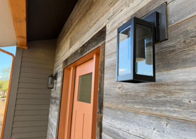 Beautiful exterior door closeup orange accent color with rustic wall paneling and modern light fixture on Custom Home with Lockoff ADU in Buena Vista by S&T Construction